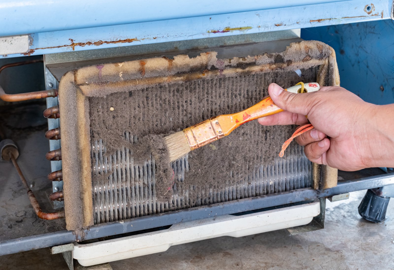ac technician cleaning a heavily dust-clogged evaporator coil with a brush to restore efficiency and airflow. ac being repaird.
